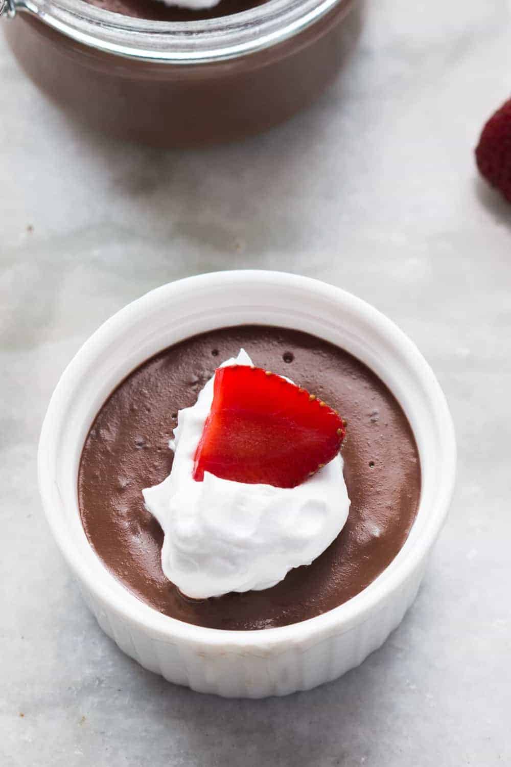 A picture of the chocolate pudding topped with whipped cream and a strawberry and served in a white bowl.