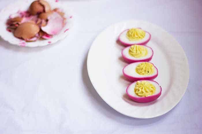 pink dyed eggs placed on a white plate with egg shells on the side