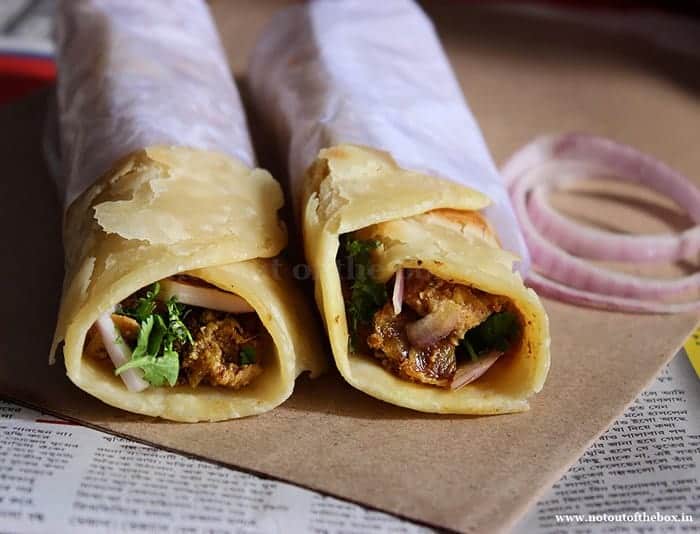 Two Kolkata Street Style Chicken Rolls and rings of onion placed on a brown paper 