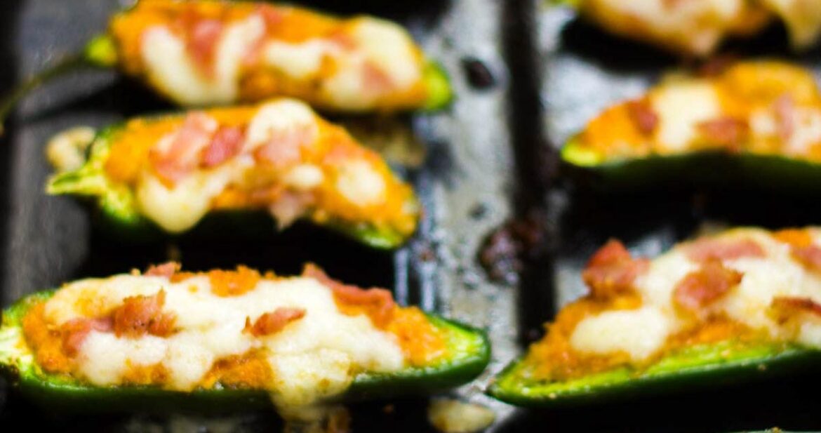 Baked jalapeno poppers lined up on a black tray.