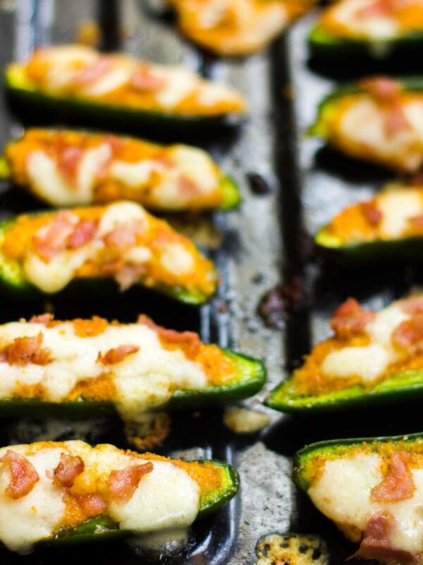 Baked jalapeno poppers lined up on a black tray.