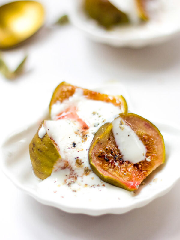 Roasted figs with cardamom yogurt served in a tiny white bowl.