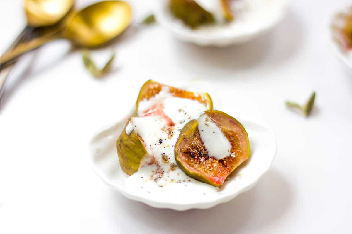 Roasted figs with cardamom yogurt served in a tiny white bowl.