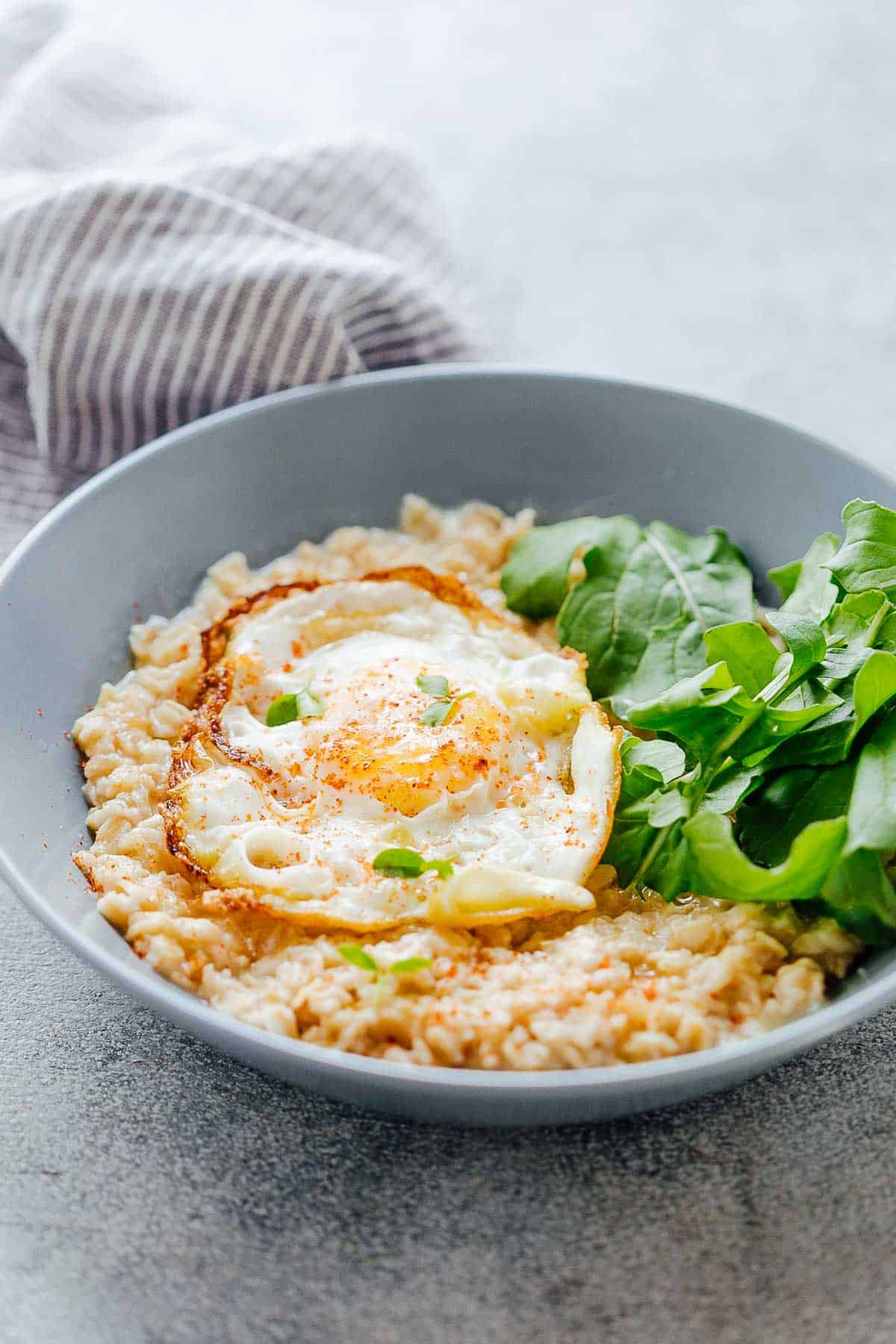 Savory Garlic Oats with Masala Fried Egg in a bowl with mixed lettuce greens