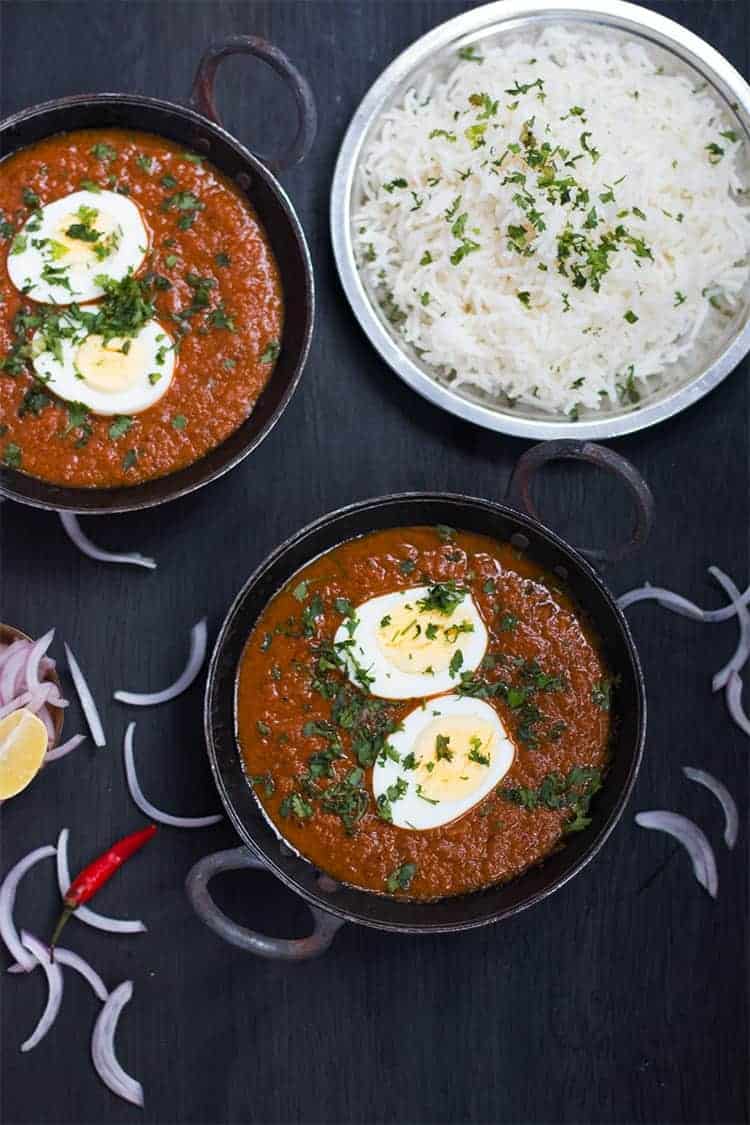egg curry served in a small black kadhai
with a plate of rice on the side