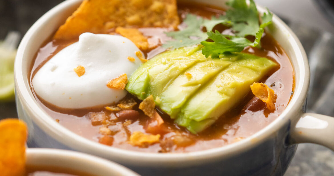 Picture of mexican soup served in a bowl topped with avocado, cilantro, sour cream and tortilla chips