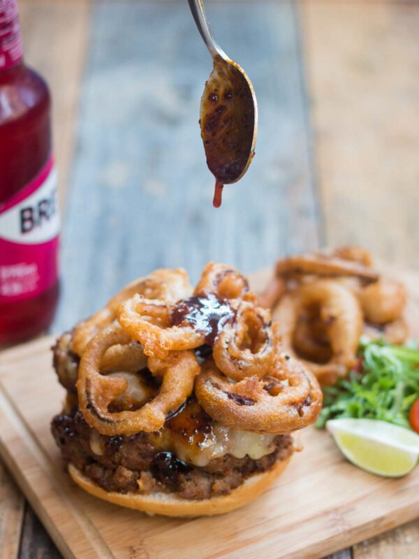 Whiskey sauce being poured over the onion rings in the burger.