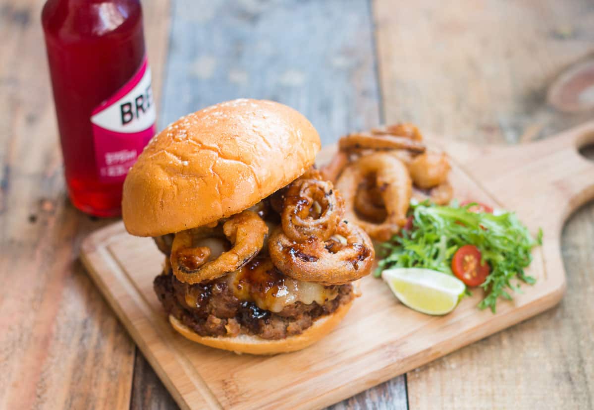 The wholesome badass burger plated with salad, onion rings and a Breezer on the side.