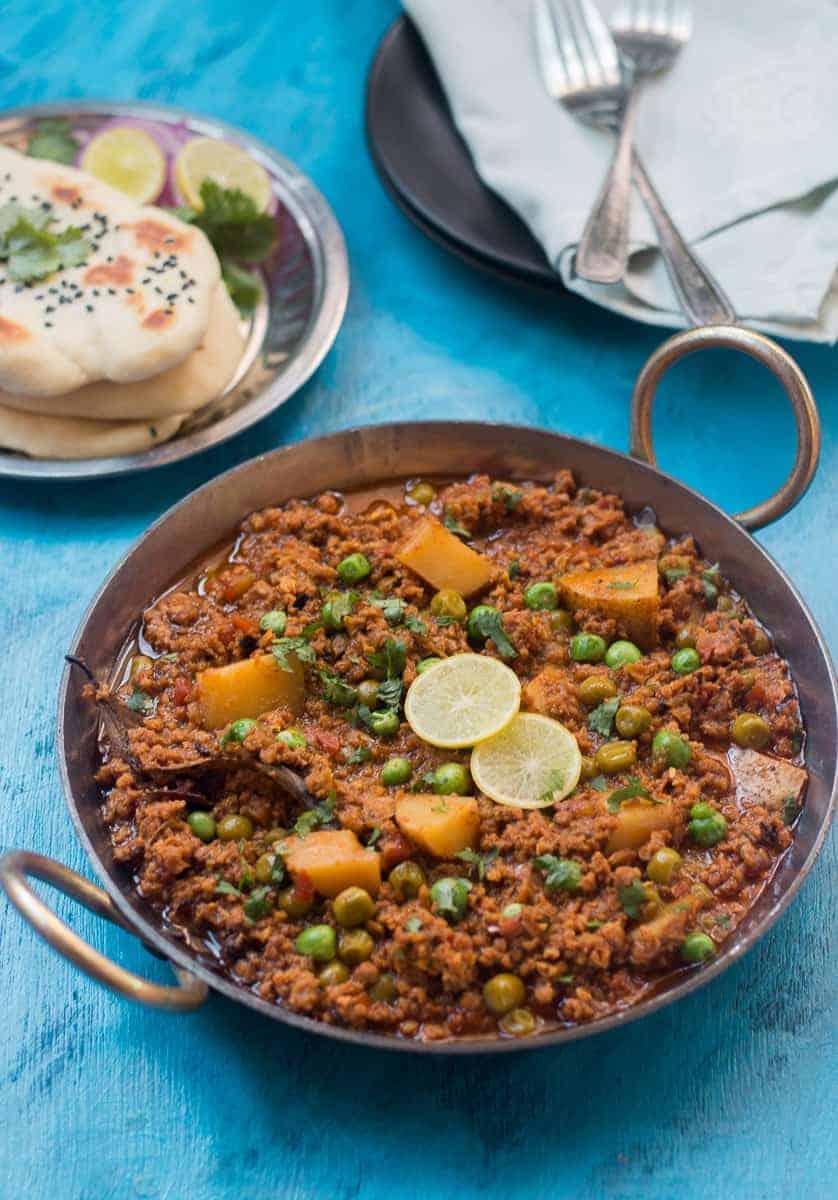 mutton keema in a kadhai with limes, chopped onion and naan on the side