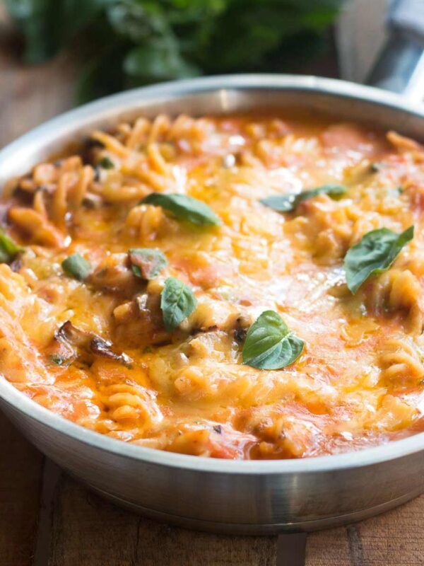 All-In Sunday Veggie Pasta layered with warm, melted cheese and garnished with fresh basil in a skillet.