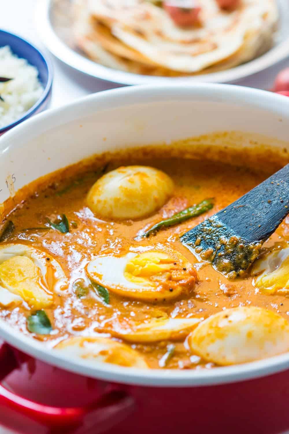 South Indian style Egg Curry is incredibly easy to make. A few spices, onions, tomatoes and coconut milk make this utterly satisfying and comforting egg curry recipe that tastes best with parathas (flatbread) and rice. Make extras because everyone will want seconds! #indian #curry #recipe #coconut #eggs South Indian Style Egg Curry in a pot with steamed rice and malabar parathas