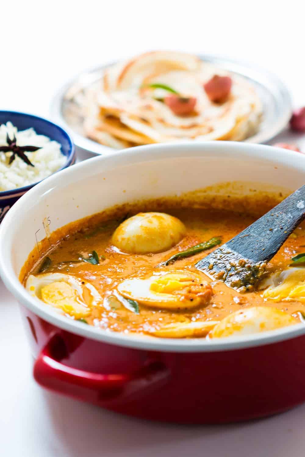 South Indian style Egg Curry is incredibly easy to make. A few spices, onions, tomatoes and coconut milk make this utterly satisfying and comforting egg curry recipe that tastes best with parathas (flatbread) and rice. Make extras because everyone will want seconds! #indian #curry #recipe #coconut #eggs South Indian Style Egg Curry in a pot with steamed rice and malabar parathas