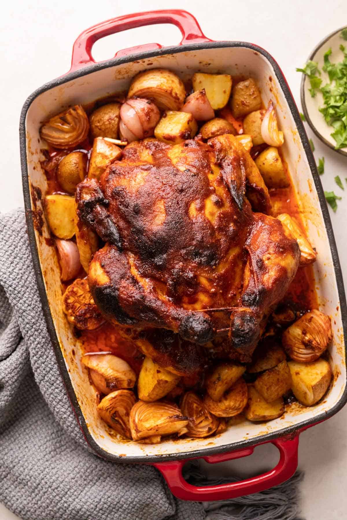 Indian roast chicken served on a bed of onions, potatoes and garlic in a red roasting pan