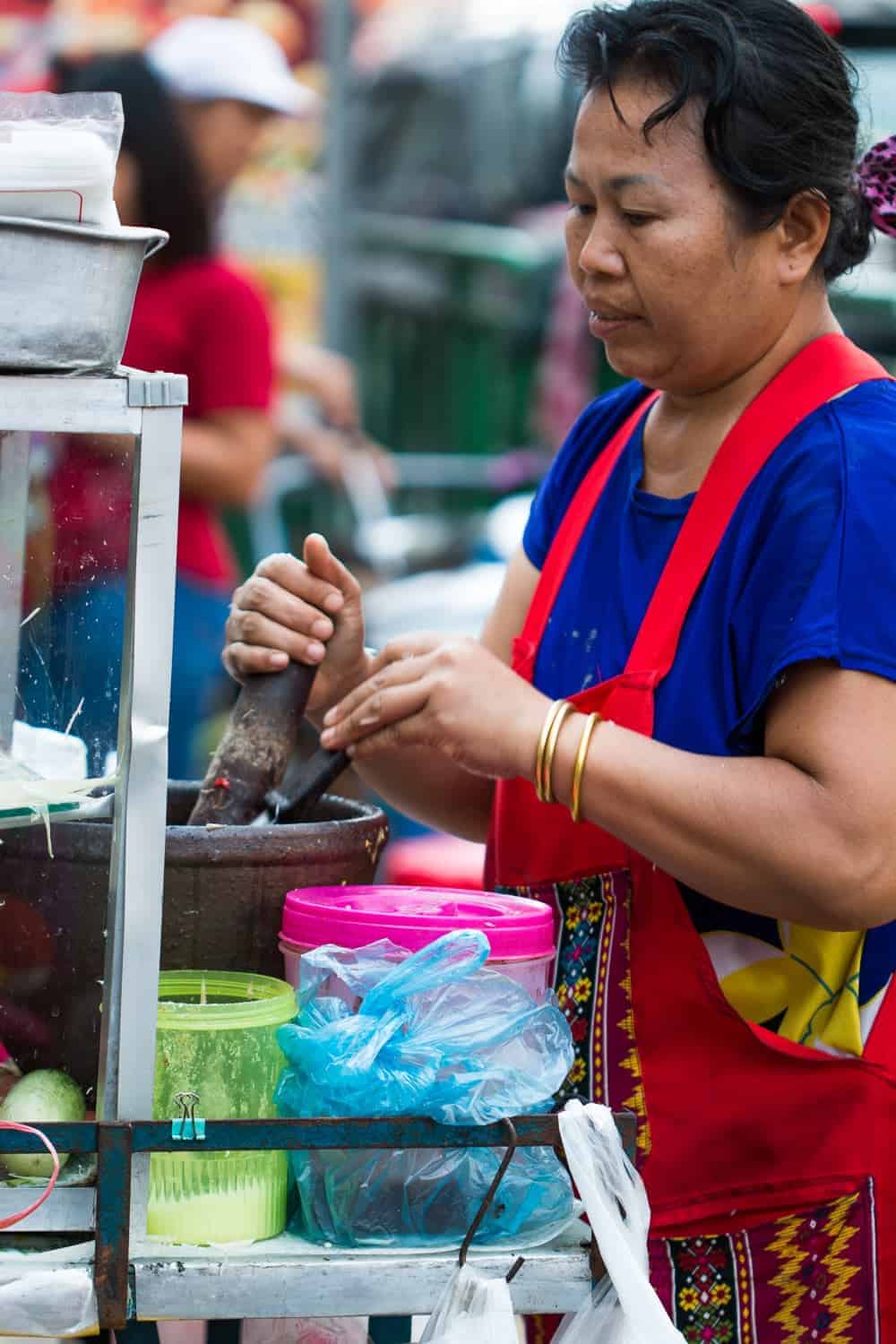 A woman in blue with a red apron cooking street food
