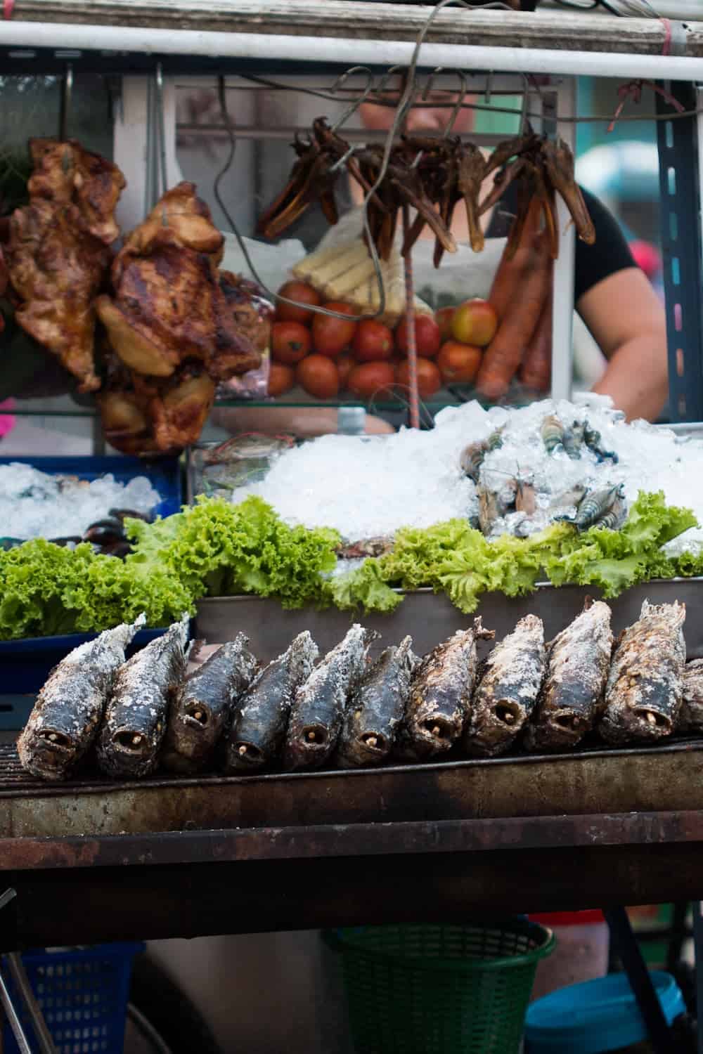 Fish, chicken, some greens and tomato placed on a street food cart