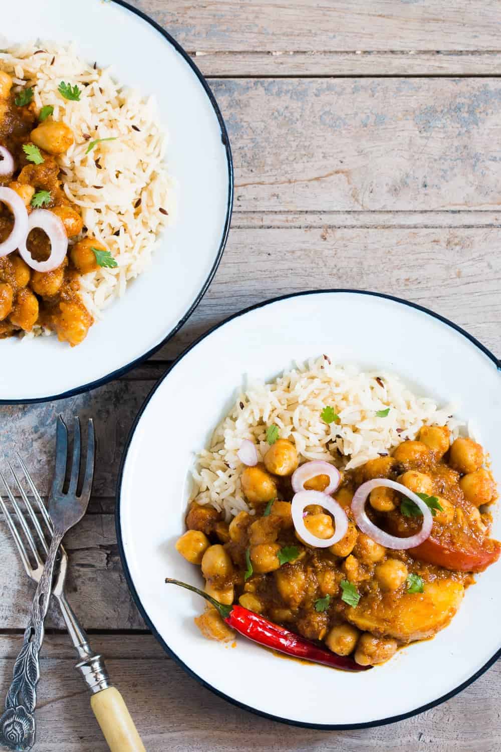 chana aloo masala with rice, cut onions and chilli on a white plate placed on a brown board
