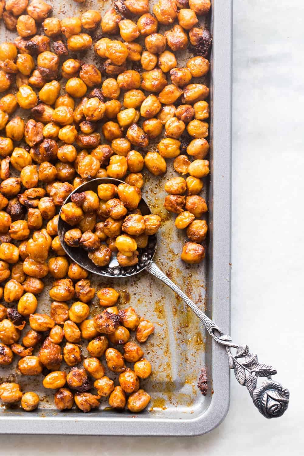 crunchy roasted indian masala chickpeas in a baking tray with a spoonful of it on the side