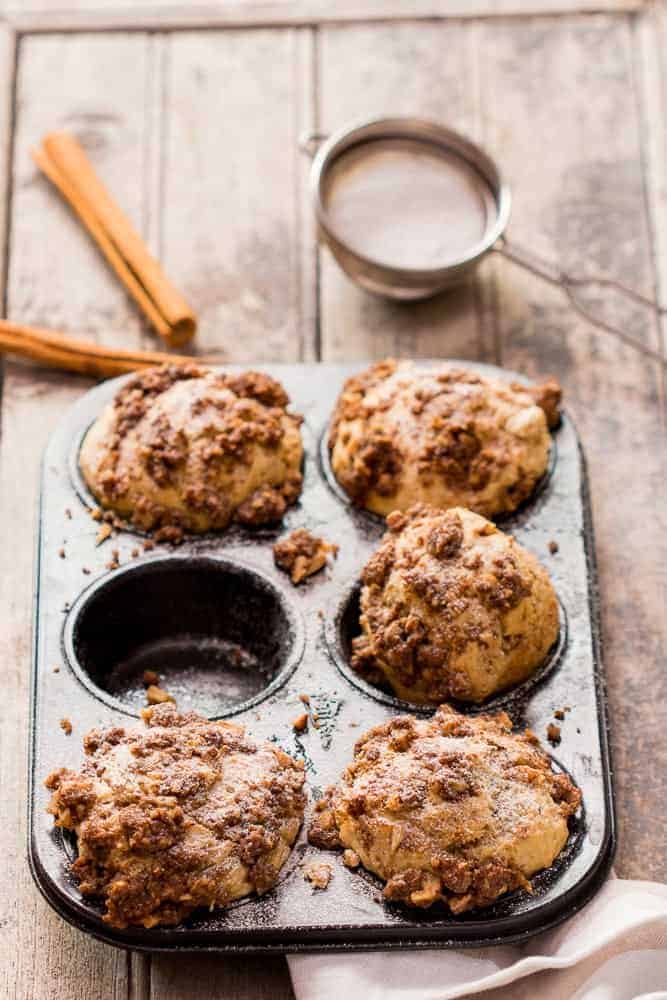 cinnamon roll muffins with crunchy streusel top in a baking tin with cinnamon sticks on the side