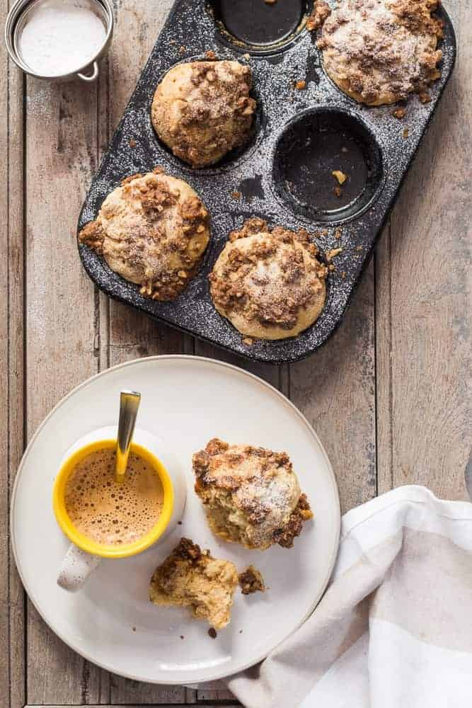 cinnamon roll muffins with crunchy streusel top in a baking tin with with a beverage and muffins in a plate
