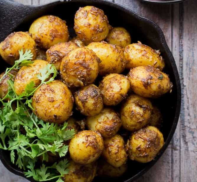 Bombay potatoes garnished with coriander and served in a black pan.