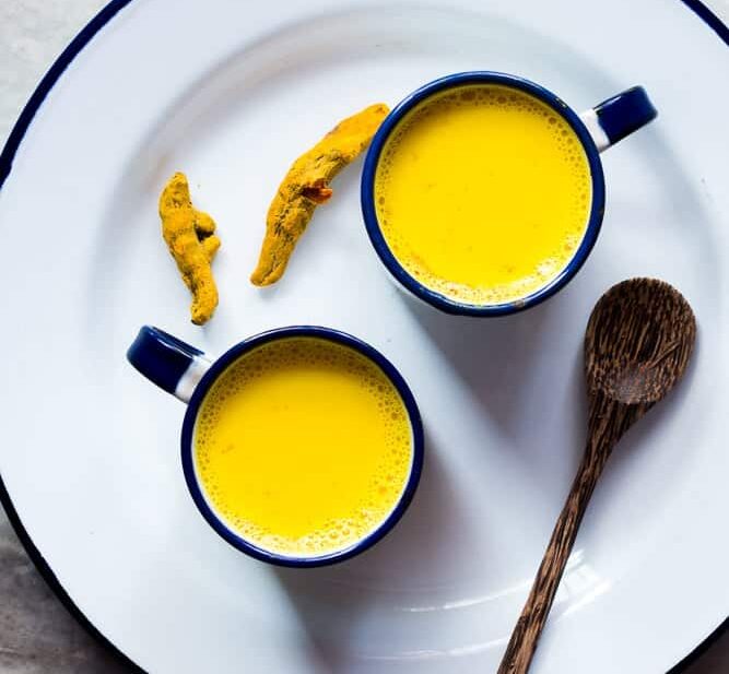 Haldi doodh served in cups kept on a white plate.