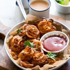 Crispy Baked Onion Pakodas (Fritters) garnished with coriander and served with sauce and chai.