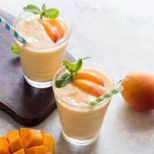 Healthy Vegan Frozen Peach Mango Smoothie garnished with mint leaves and served with straws.