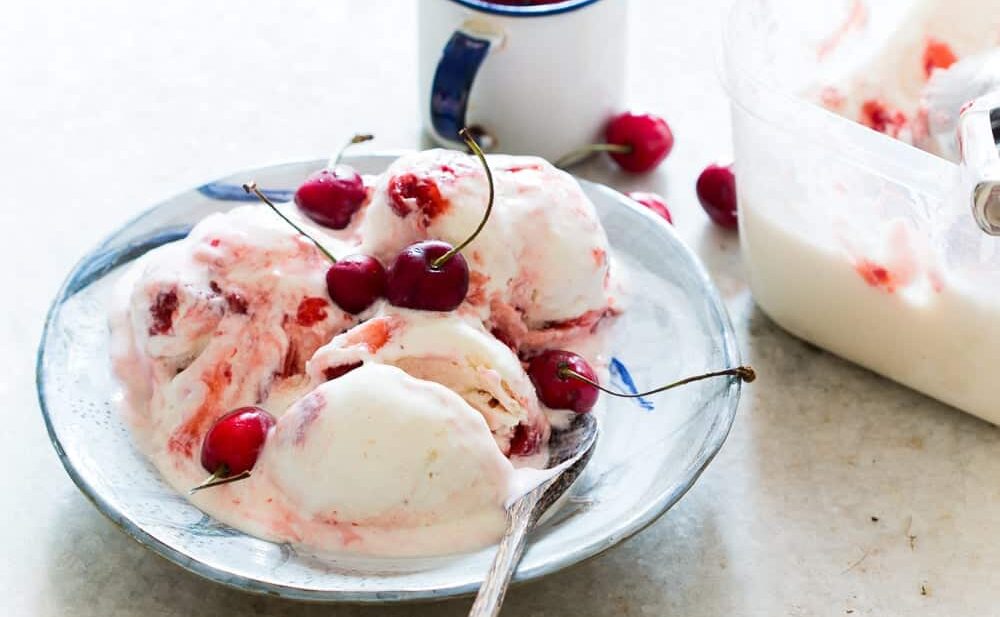 Lychee Cherry Swirl Ice Cream garnished with cherries and served on a white plate.