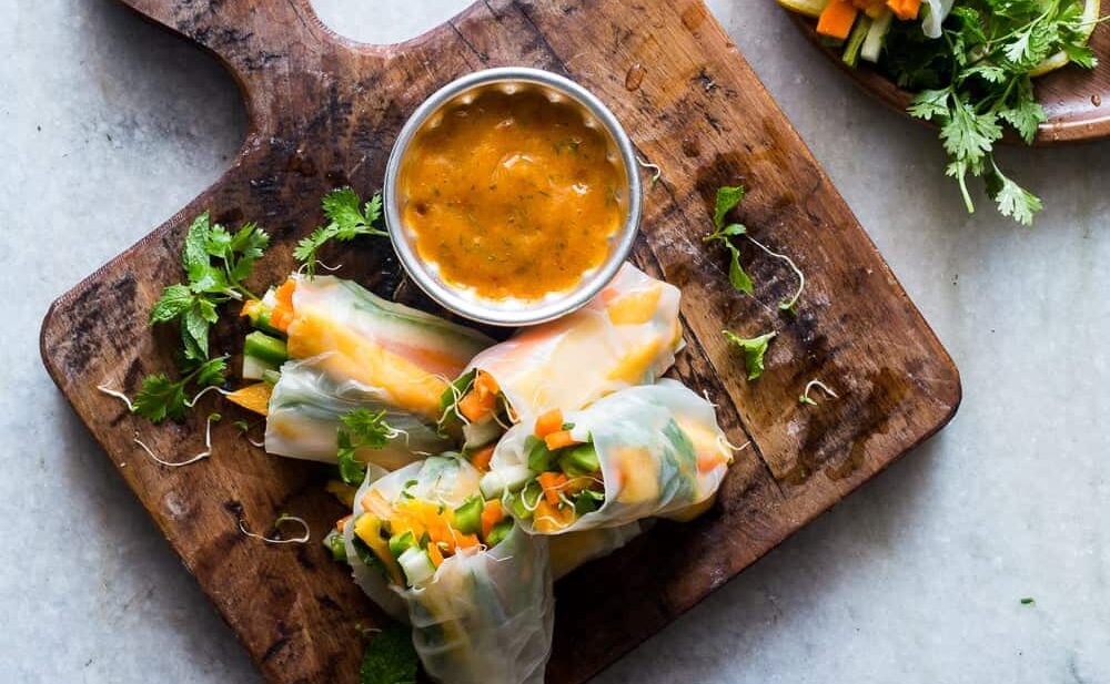Mango Bell Pepper Rice Paper Rolls with Mango Cilantro Dipping Sauce served on a wooden board.