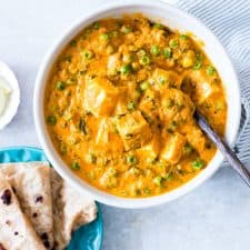Creamy Matar Paneer Curry served in a white bowl with a side of paranthas.