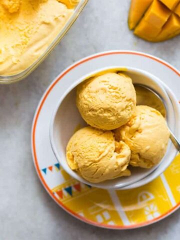 Three scoops of Homemade Mango Cheesecake Ice Cream served in a white bowl.