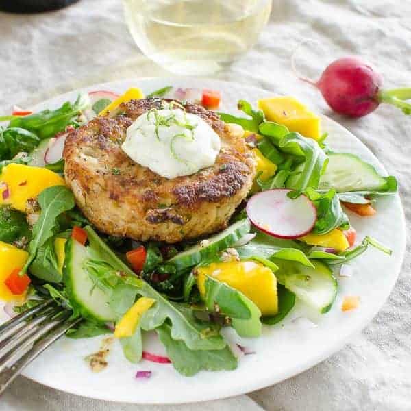 Mango crab cakes with a mango lettuce salad on a white plate with a fork