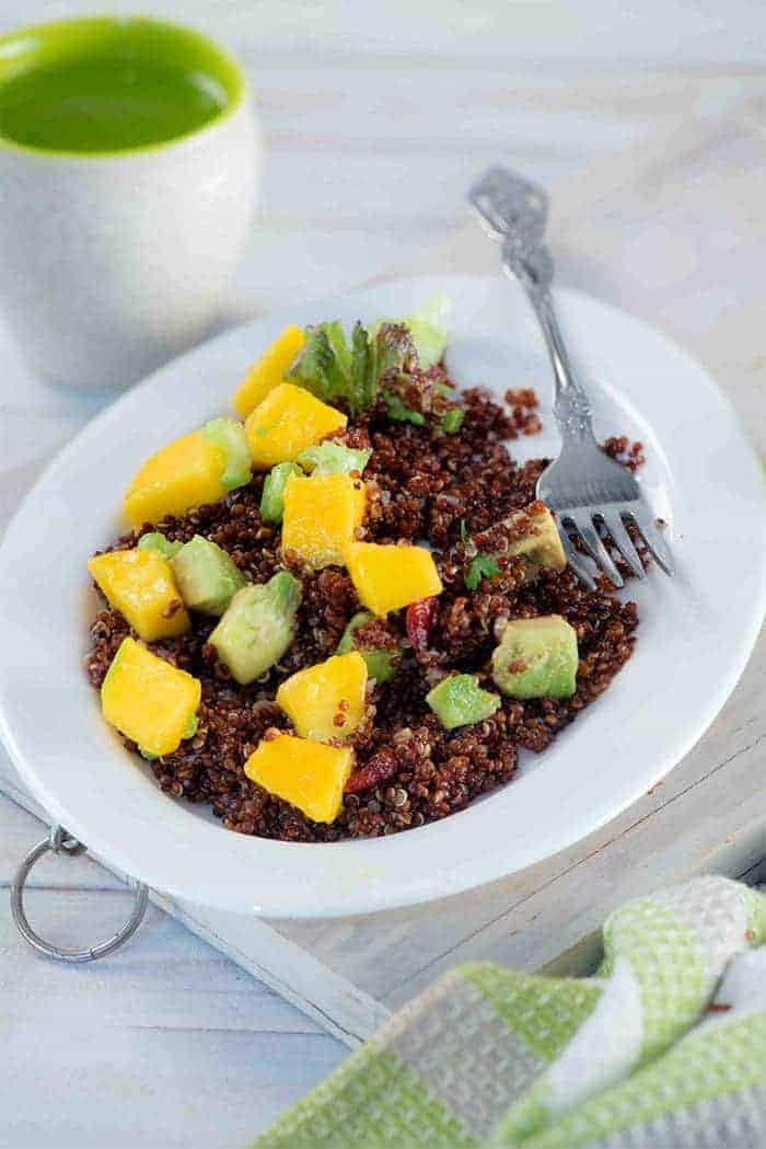Red quinoa mango salad in a white deep plate with a fork and a glass of water