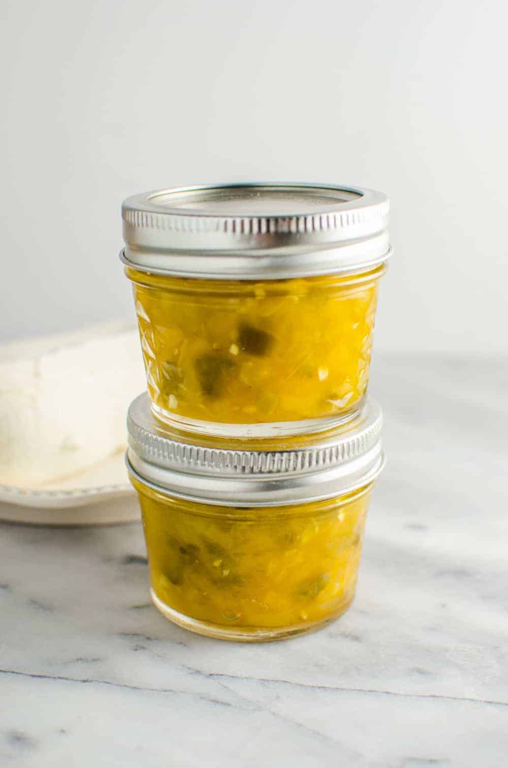 Mango jalapeno jam stored in two glass jars with lid, stacked on top of the other