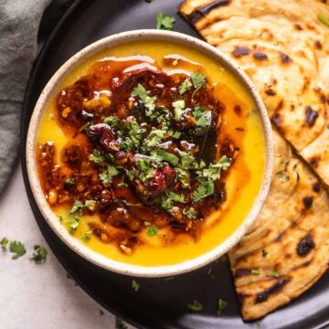 Dal tadka served in a bowl kept on a black plate with tandoori rotis on the side