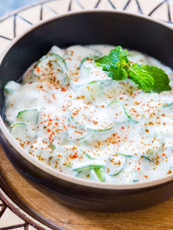 Indian Spiralized Cucumber Mint Raita garnished with some mint, masala and served in a black bowl.