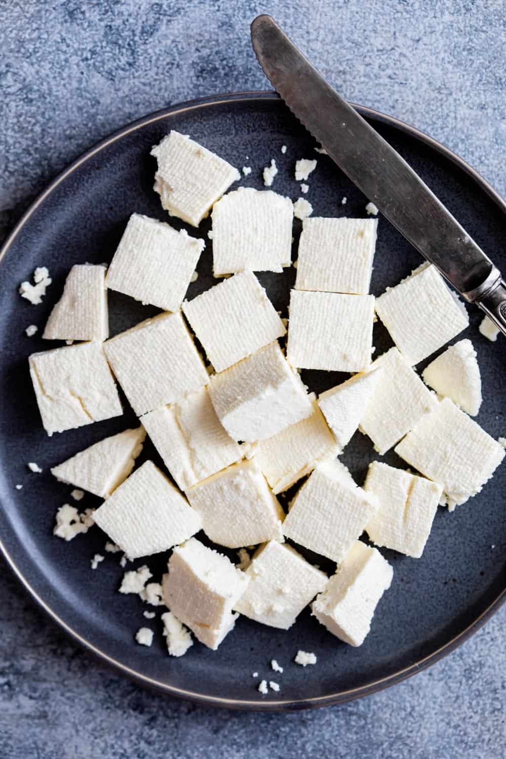 Learn how to make paneer at home. Cubes of paneer on a dark plate