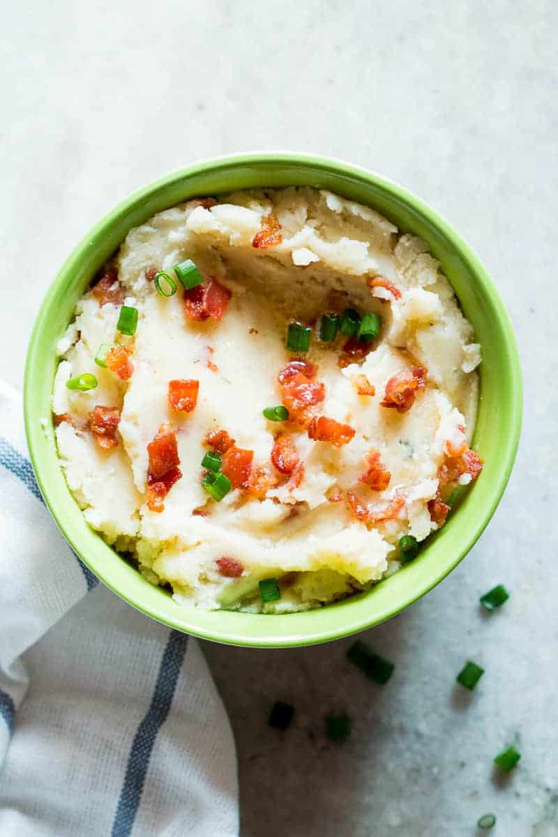 Slow cooker mashed potatoes topped with bacon served in a green bowl