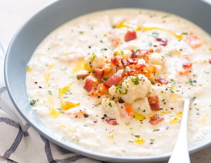 Creamy Cauliflower Chowder topped with bacon, olive oil and served in a bowl.