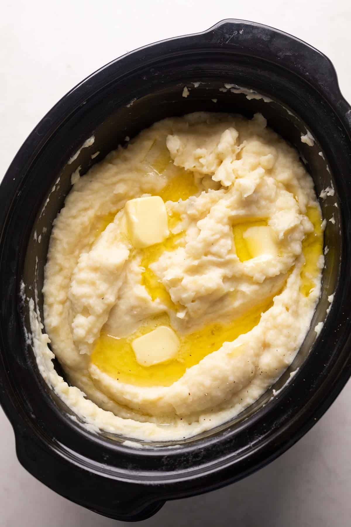 Mashed potatoes cooked and served in the slow cooker with blobs of butter on top