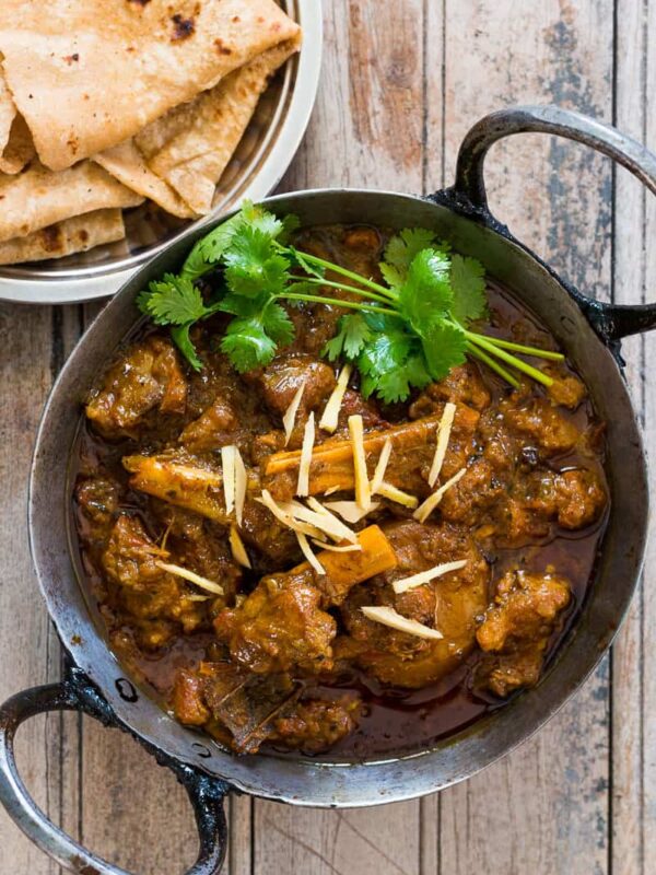 Mutton curry garnished with coriander, ginger and served in a kadhai alongside paranthas.