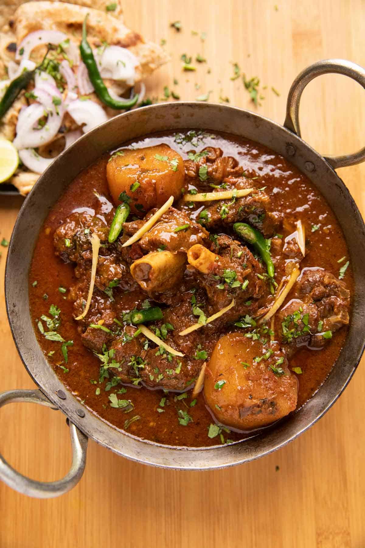Mutton Curry served in a kadhai with tandoori roti and onions on the side