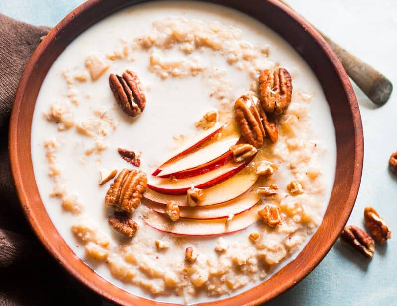Oatmeal topped with pecans, honey, fresh apple and served in a bowl.