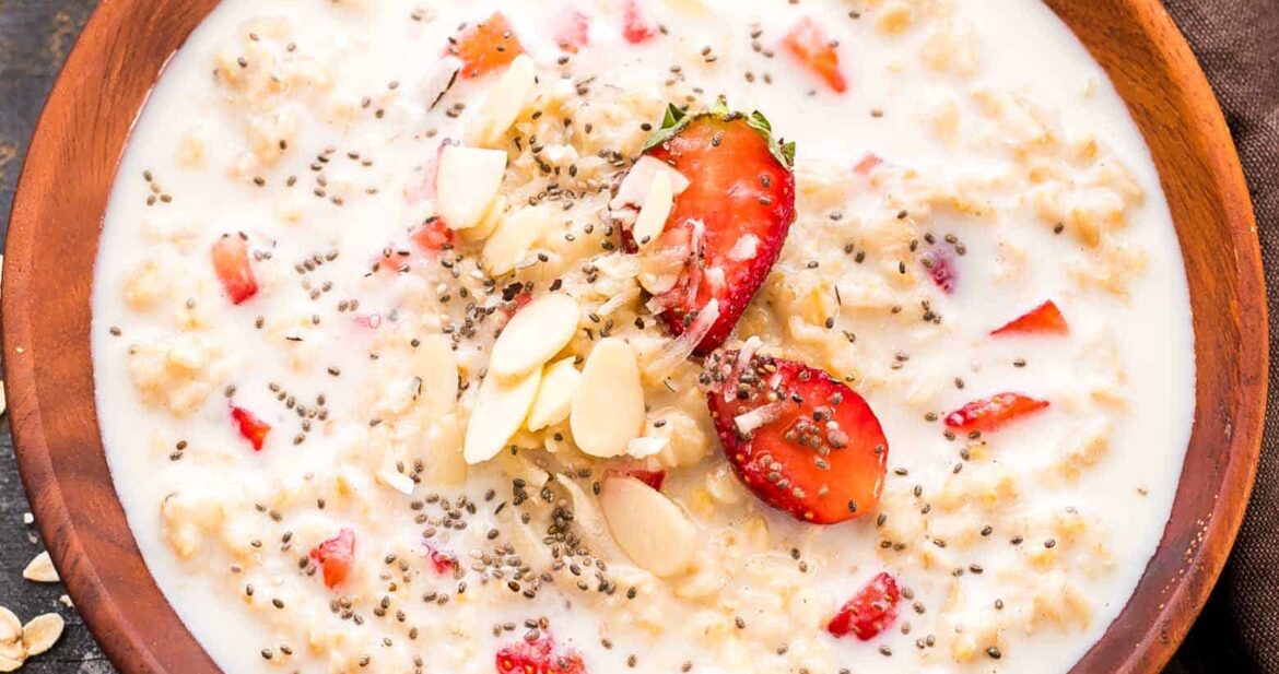 Healthy Strawberries and Cream Breakfast Oatmeal drizzled with honey, chia seeds and served in a wooden bowl.