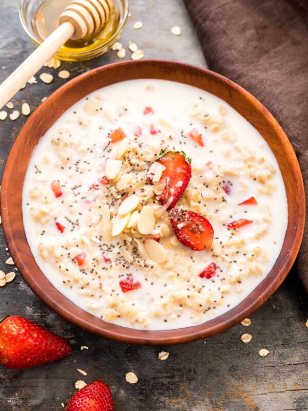 Healthy Strawberries and Cream Breakfast Oatmeal drizzled with honey, chia seeds and served in a wooden bowl.