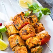 Paneer tikka skewers garnished with mint, lemon and served on a white plate.