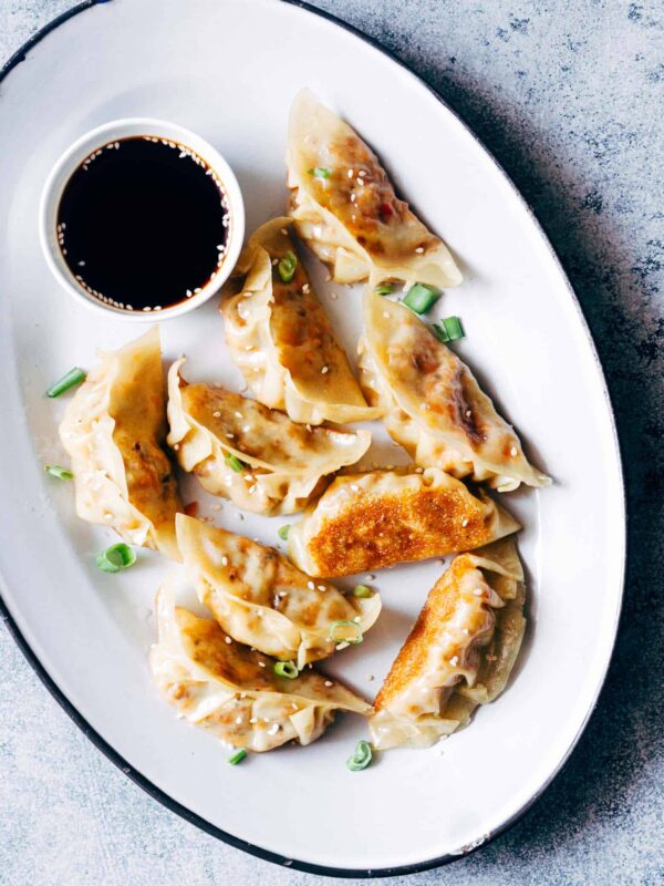 Vegetarian Gyoza Potstickers with Carrot and Paneer served with a dipping sauce on a white plate.