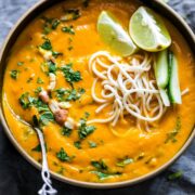 Thai Ginger Carrot Soup garnished with lemon, crushed peanuts, noodles and cilantro and served in a woebegone bowl.