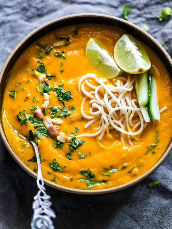 Thai Ginger Carrot Soup garnished with lemon, crushed peanuts, noodles and cilantro and served in a black bowl.