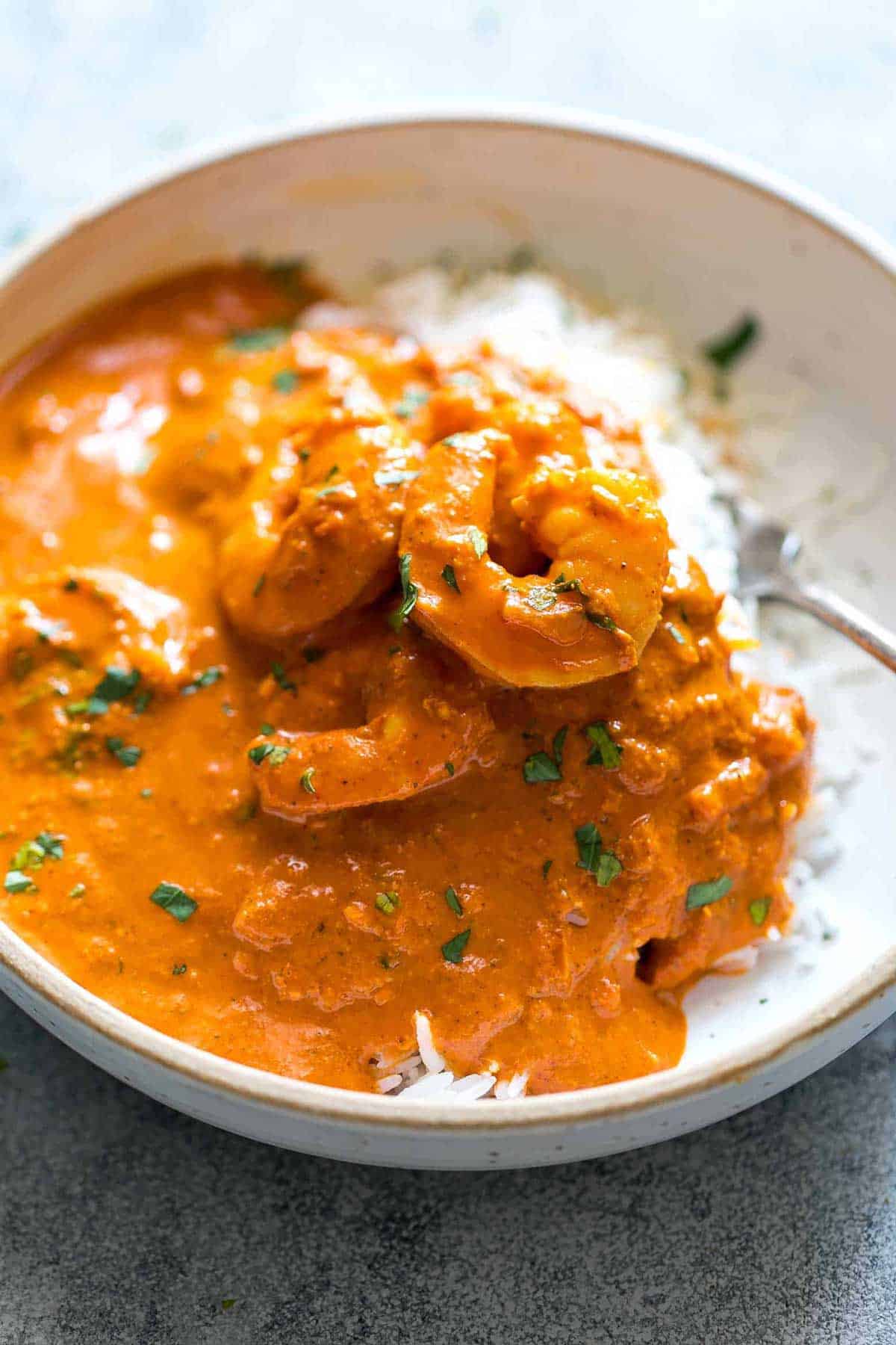 Goan prawn curry ladled over steamed rice and served in a white bowl with a fork on the side